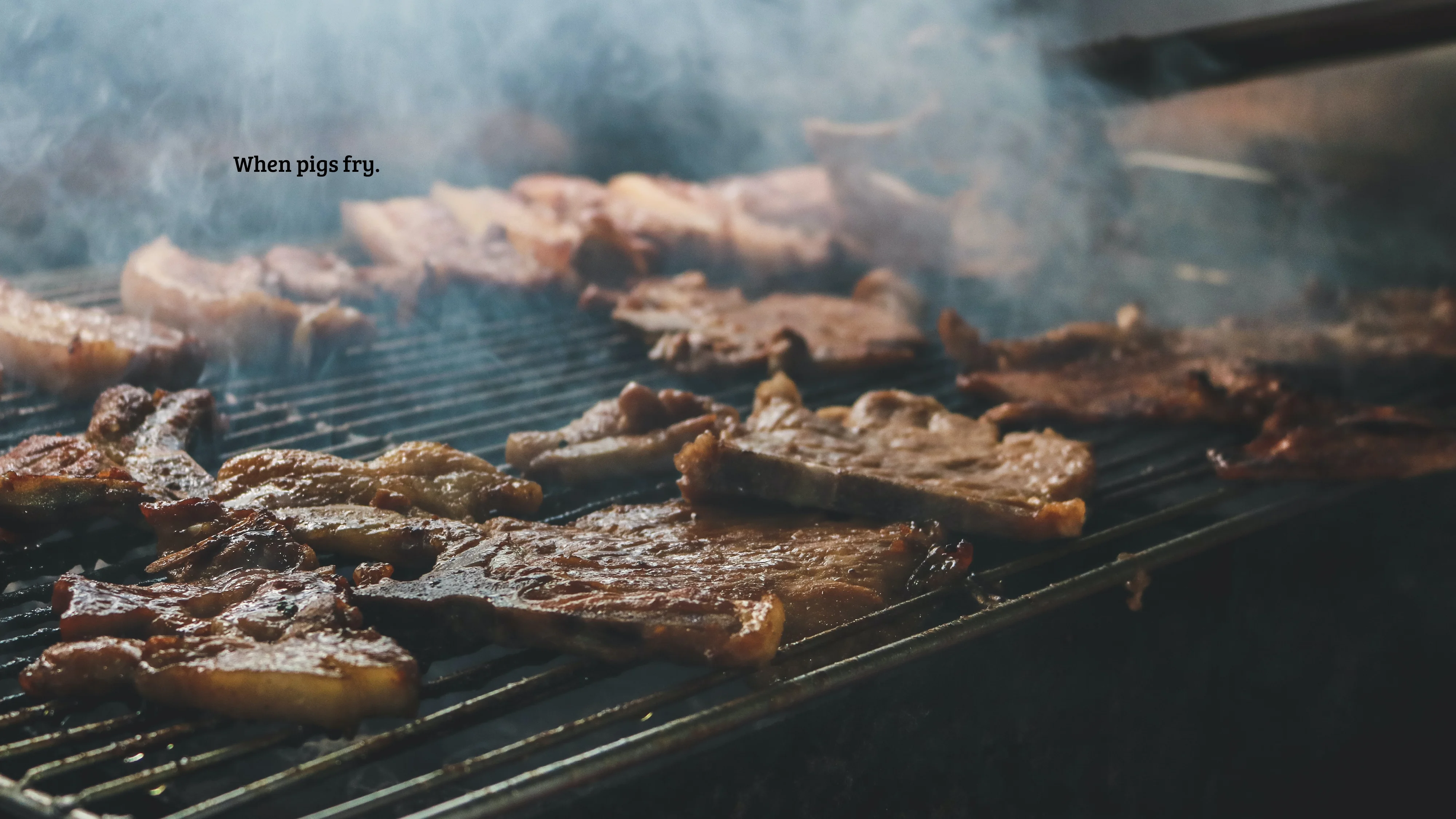 Grilled meat sizzling over a dark barbecue grill. Text: “When pigs fry.”