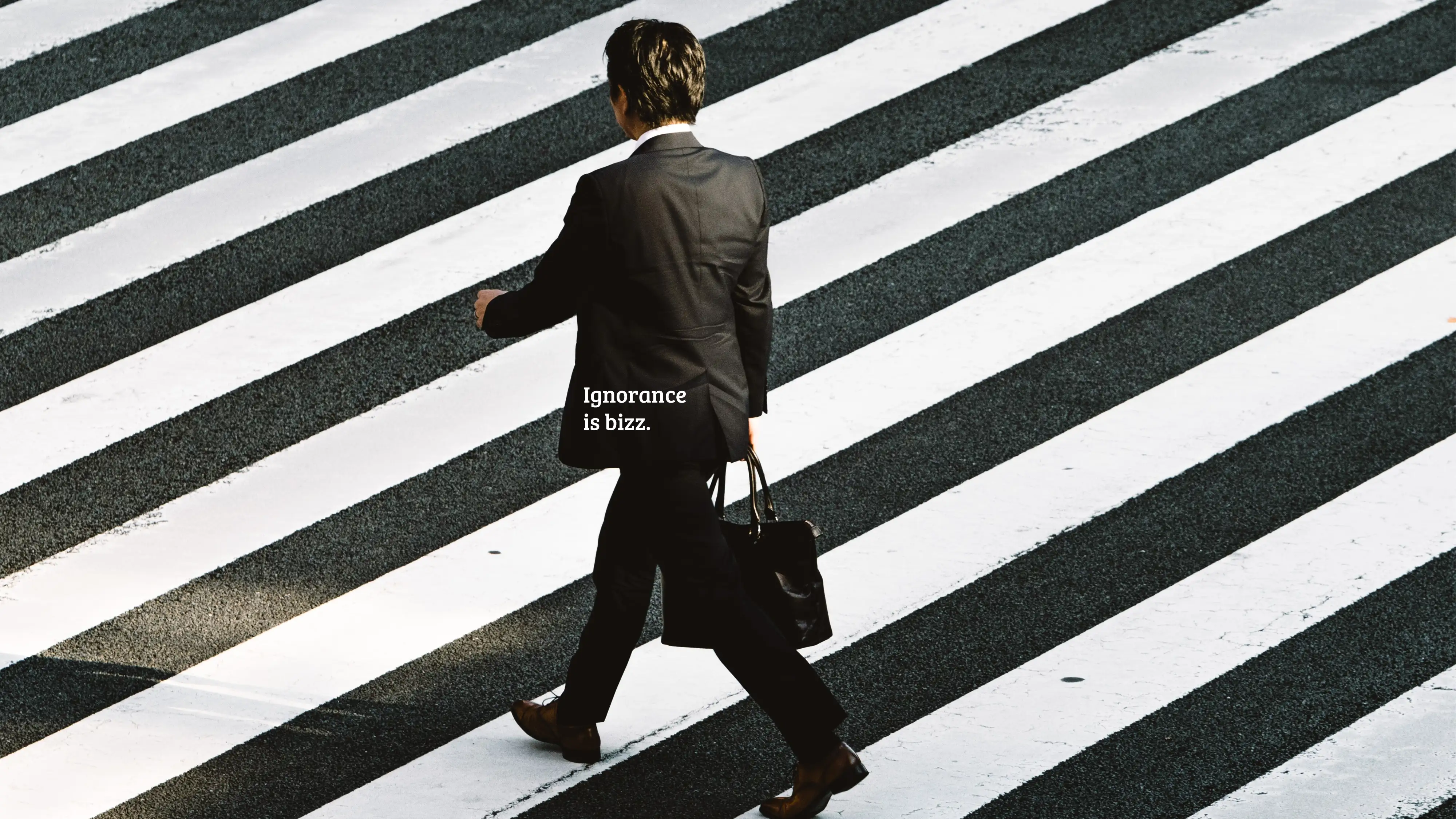 A businessman in a dark suit walks across a bold black-and-white striped crosswalk. Text: “Ignorance is bizz.”