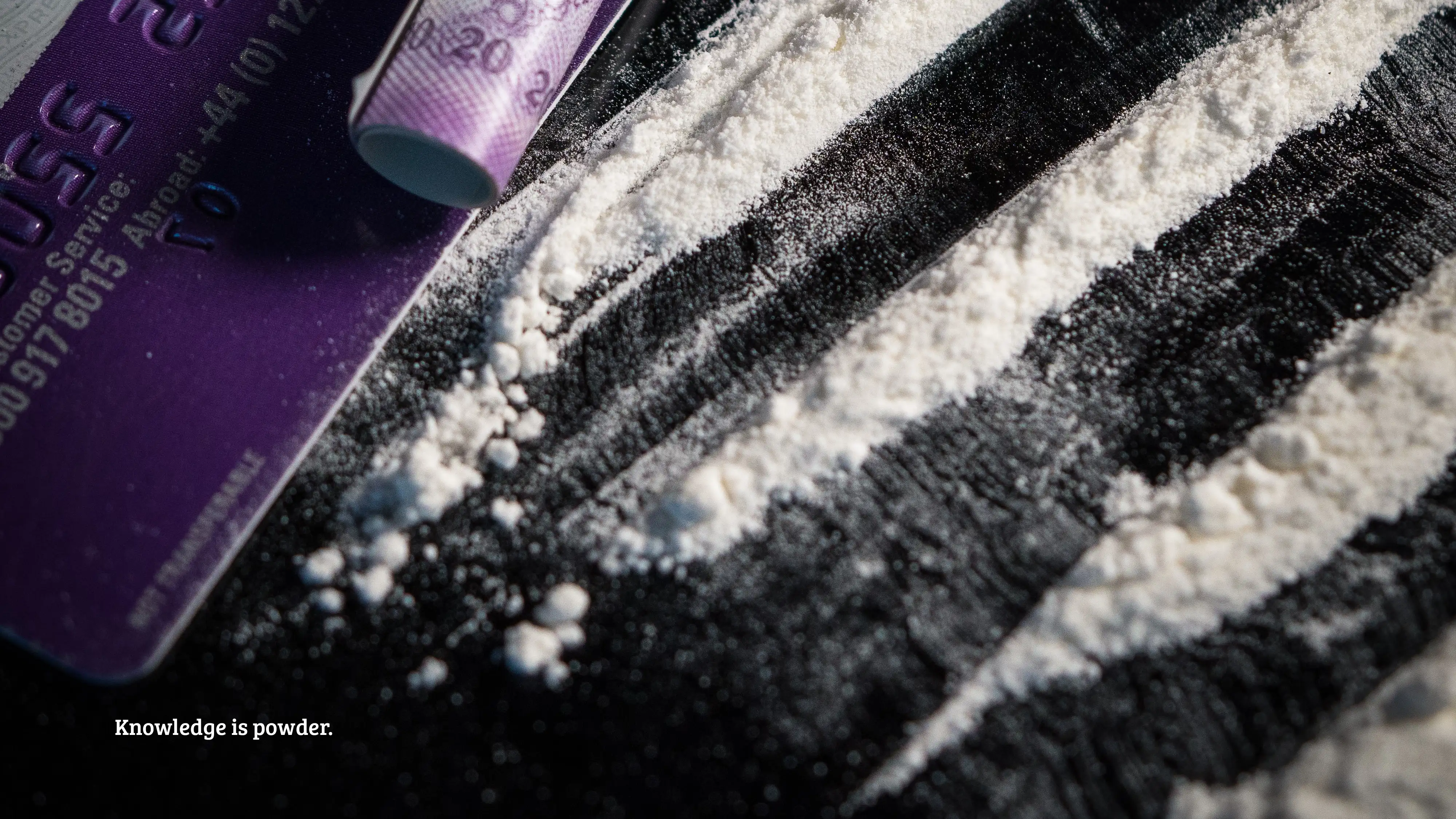 A purple and black card against a simple background and white powder. Text: “Knowledge is powder.”